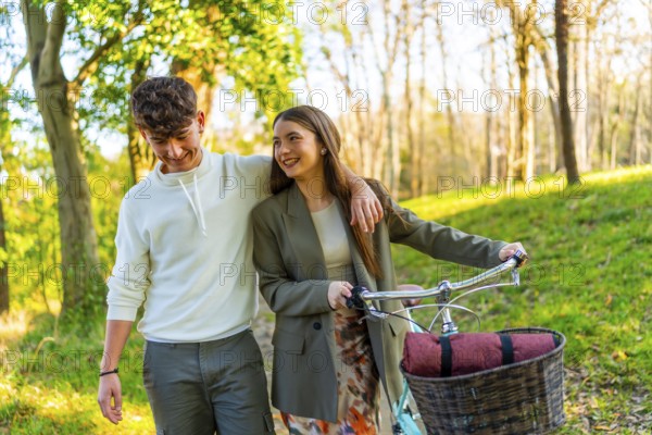 Smiling young couple walking in a sunlit park, sharing a moment together. Woman pushing a bicycle