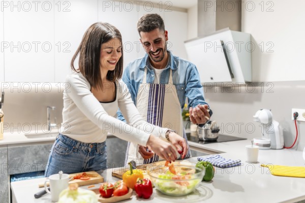 Young couple smiling and preparing a vibrant, healthy salad together in their modern kitchen,