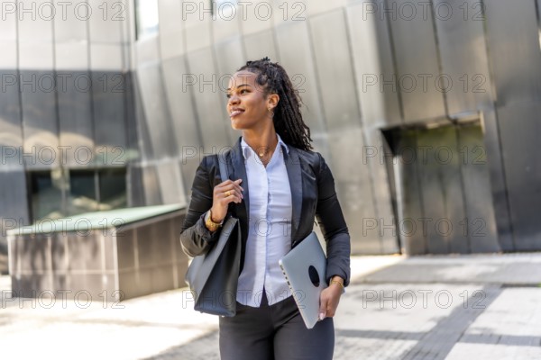 Portrait of a latin businesswoman walking distracted carrying laptop in the city next to a modern