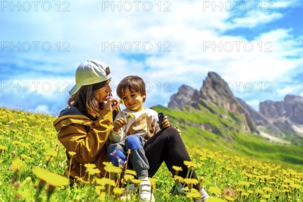 Tourists enjoying summer in the italian alps, smelling wildflowers with the odle mountains in the