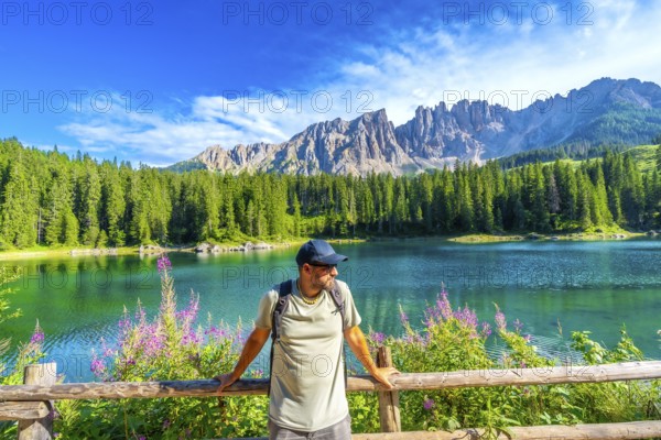 Hiker admiring the stunning turquoise waters of lake carezza with the latemar mountain range in the