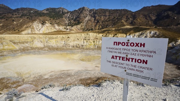 Warning sign in front of volcanic crater in sunny mountainous landscape, volcanism, volcanic