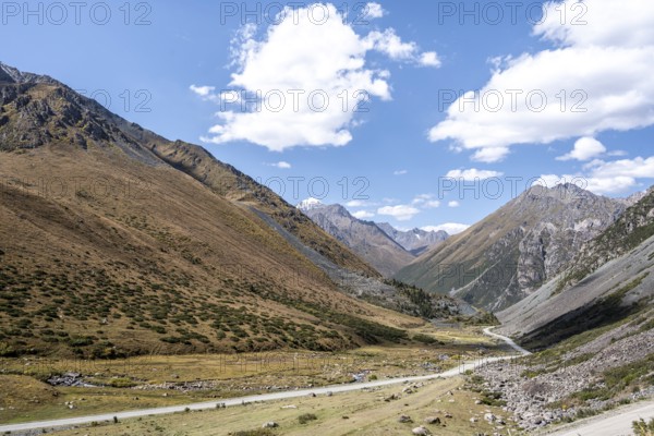 Gravel track in a valley, picturesque mountain landscape with white mountain peaks, Tian Shan