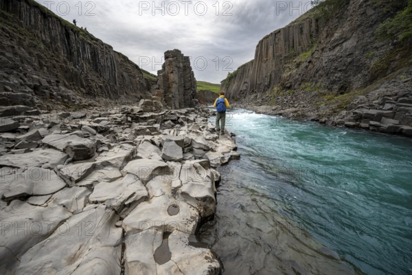 Tourist standing by the river in Stuðlagil Canyon, turquoise blue river between basalt columns,