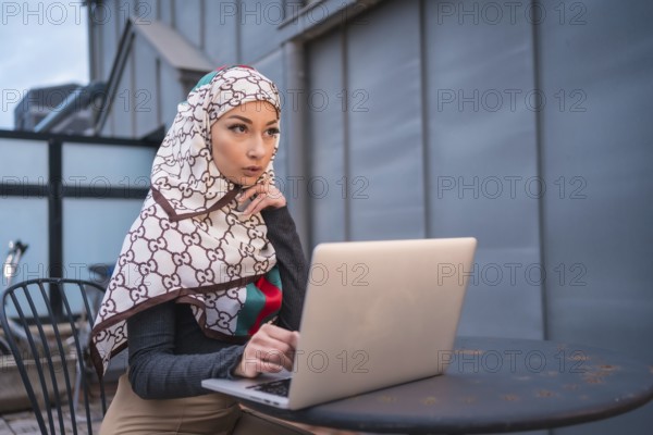 Arab girl with a white veil at the computer on the terrace of a coffe shop, contrabass with the