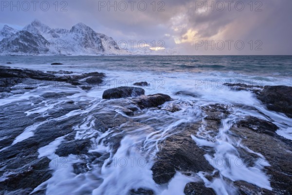 Beach of Norwegian sea on rocky coast in fjord on sunset in winter. Vareid beach, Lofoten islands,