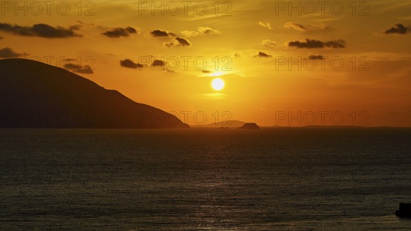 Sunset over the sea with sunbeams and an island on the horizon, warm yellow tones dominate, sunset,