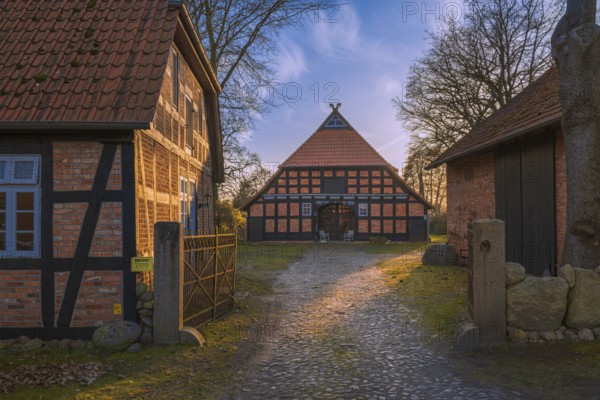 View of a courtyard entrance with a half-timbered farmhouse behind it in the evening light,