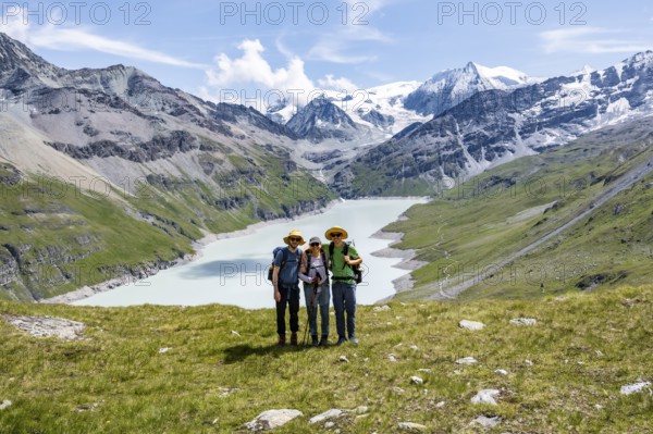 Three friends, mountaineers in front of a blue mountain lake, reservoir Lac des Dix, behind