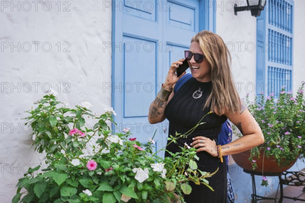 A joyful middle-aged woman with straight hair and a curvy Latin figure chats on the phone in front