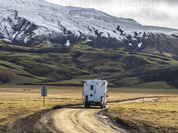 Pickup camper on gravel road, early snow on mountain range, along road Landmannaleid F225,