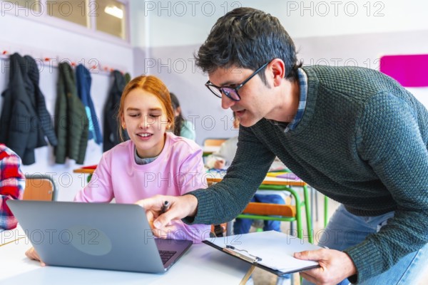 Teacher assisting female student using laptop during lesson in classroom, promoting interactive