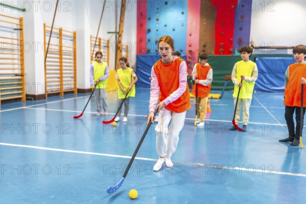 Group of elementary school students wearing orange and yellow vests playing floorball in a gym