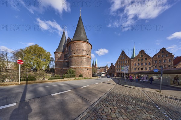 Lübeck Holstentor, side view, pedestrian crossing, cobblestone pavement, blue sky with fair weather