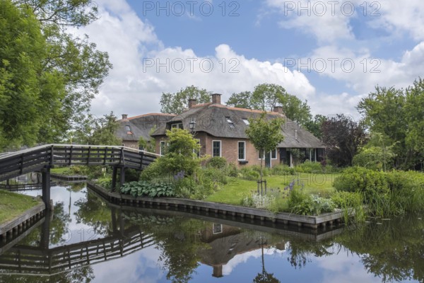 Large house with water reflection and wooden bridge in a peaceful, natural setting, Giethoorn,