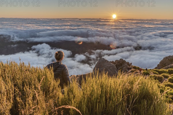 A hiker watches the sunset over a sea of clouds from a mountain top, Pico Ruivo, Madeira, Portugal,