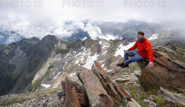 Mountaineer sitting on a rock, cloudy mountain landscape at the summit of Lasörling, view to Berger