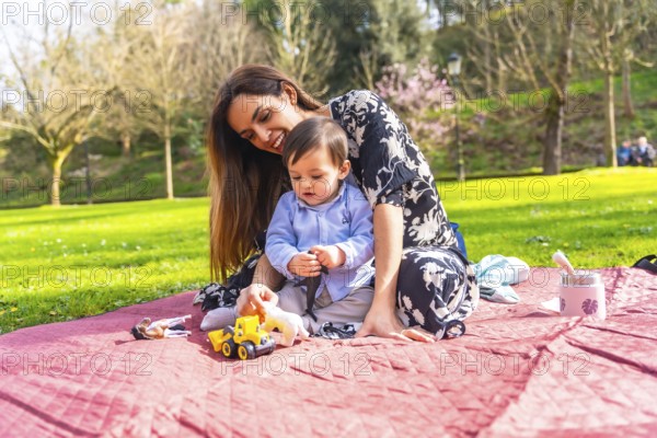 Mother and baby enjoying quality time together, playing with toys during a sunny picnic in a park