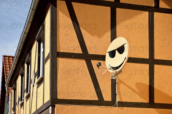 Satellite dish with smiley on a house wall in Langenstein, Halberstadt, Saxony-Anhalt, Germany,