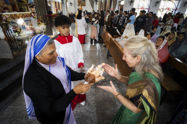 A priest holds an idol of baby Jesus Christ as devotees kiss the idol during a Christmas day sermon