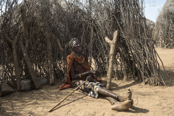 Old woman sitting in front of a fence made of wooden sticks and small tree trunks, Karo ethnic