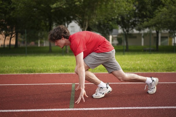 Side view full length of a caucasian young male runner in the starting line of a track ready to