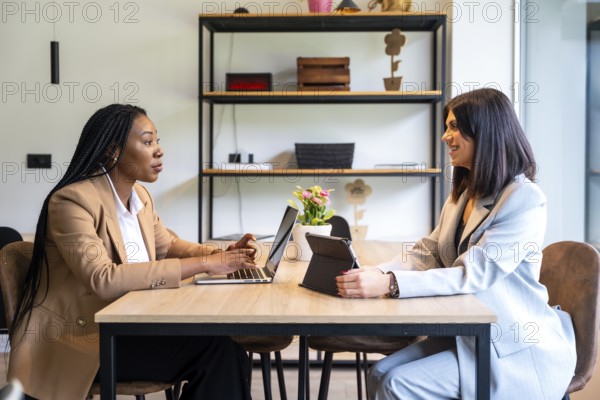 Two businesswomen are working together on a project using a laptop and tablet in a hotel lobby