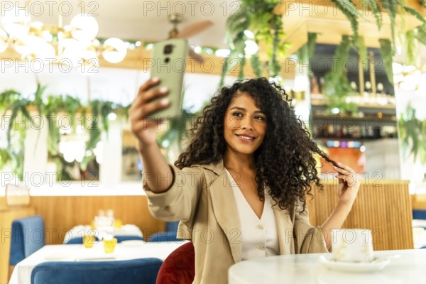 Sensual and happy latin woman taking selfie while touching her long curly hair sitting alone in a