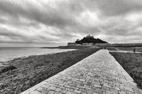 Walker, cobbled causeway, St Michael's Mount, tidal island with castle, dramatic cloudy sky,