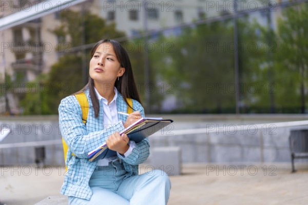 Portrait three quarter length of a beauty Asian student writing notes sitting on the campus looking