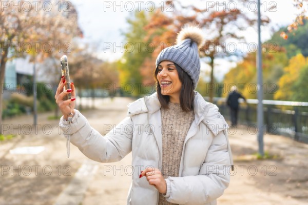 Woman wearing warm clothes and woolly hat smiling while talking during video call with mobile phone