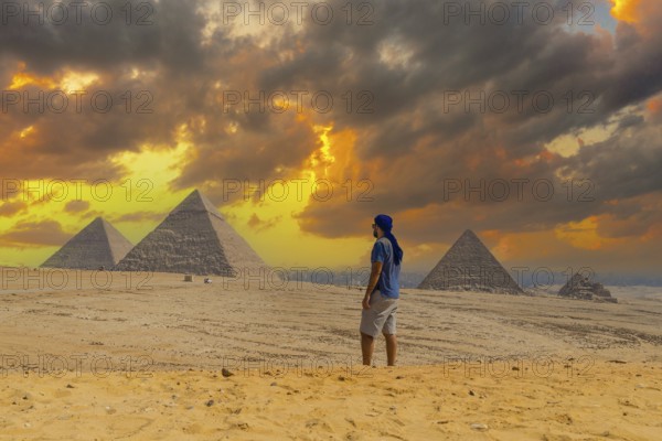 A young man in a blue turban walking next to the Pyramids of Giza, the oldest Funerary monument in
