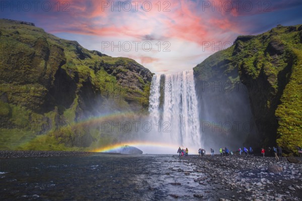 Group of tourists looking at the beautiful rainbow at the impressive Skogarfoss waterfall in