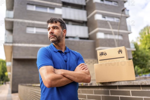 Portrait of a confident delivery man with arms crossed standing looking away next to parcels in the