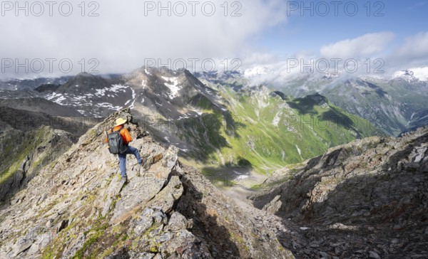 Mountaineer on a steep rocky ridge, on the summit of the Lasörling, view of the mountain panorama