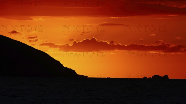 Dramatic sunset over the sea with a silhouetted island and a bright orange sky, sunset, Kassos,