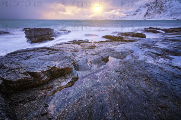 Beach of Norwegian sea on rocky coast in fjord on sunset in winter. Vareid beach, Lofoten islands,
