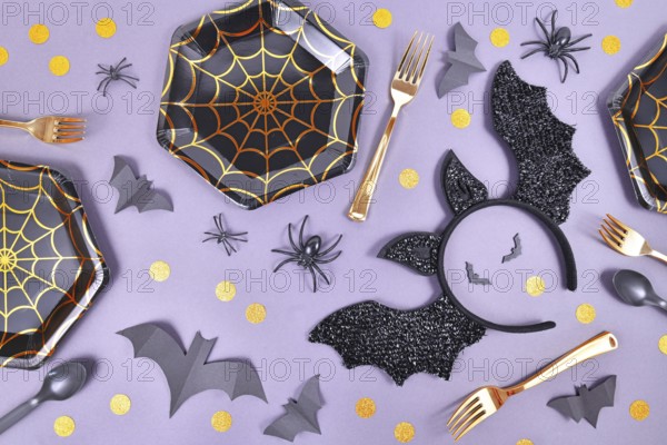 Halloween party flat lay with spider web plates, costume bat headband, spiders and confetti on