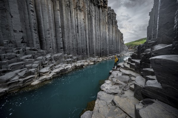 Tourist standing by the river in Stuðlagil Canyon, turquoise blue river between basalt columns,