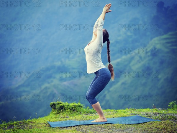 Young sporty fit woman doing yoga asana Utkatasana (chair pose) outdoors in mountains Himalayas in