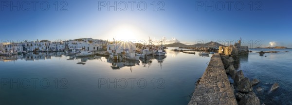 Panorama, fishing boats in the harbour of Naoussa at sunset, reflected in the sea, sun star, ruins