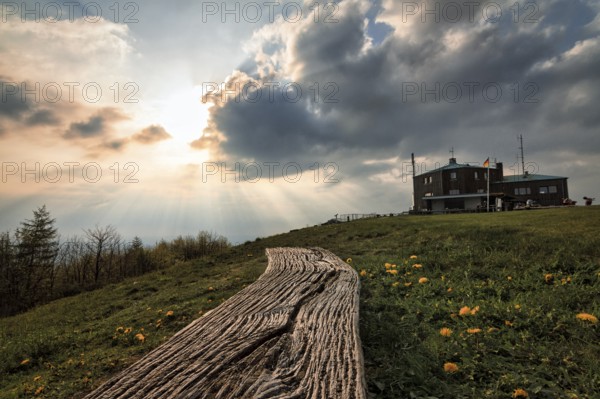 Simple bench in a meadow, illuminated by evening sun, sunbeams behind thunderclouds, mountain top