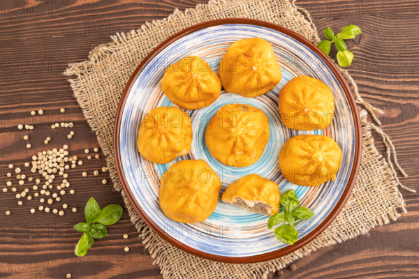 Fried manti dumplings with pepper, basil on brown wooden background and linen textile. Top view,