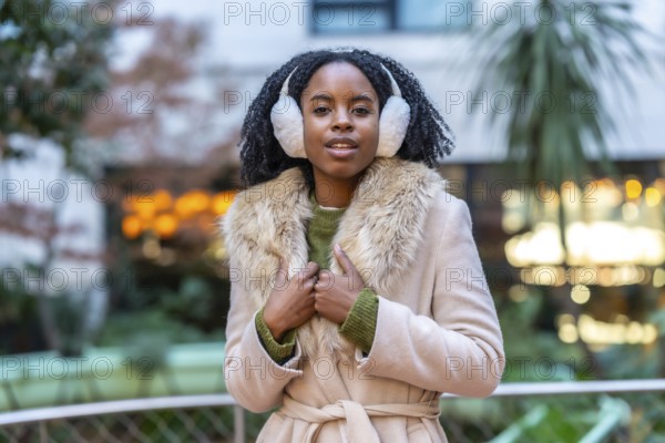 Fashionable young woman enjoys winter day in the city, wearing stylish earmuffs and a warm coat