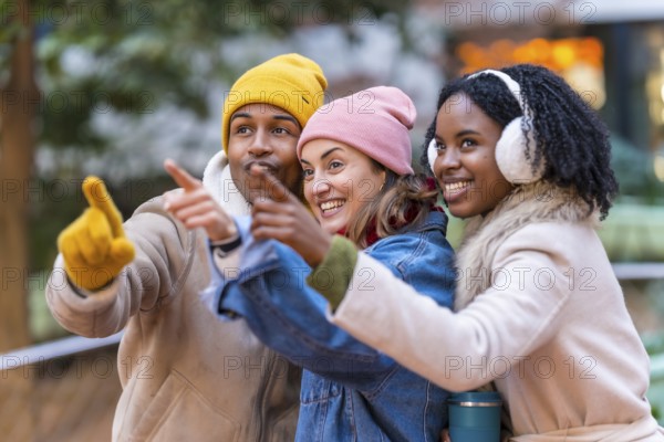 Three happy multi ethnic friends wearing winter clothes pointing their fingers at something