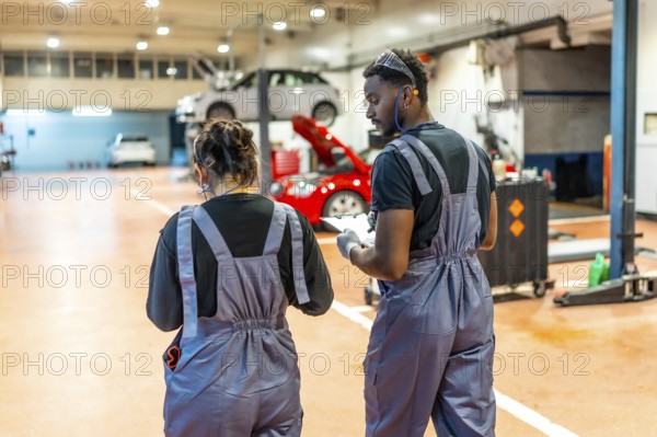 Two auto mechanics walking and reviewing notes on a clipboard in a professional garage, surrounded