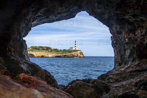 Portocolom lighthouse framed by the rocky opening of the arc natural cave, with blue sea and sky in