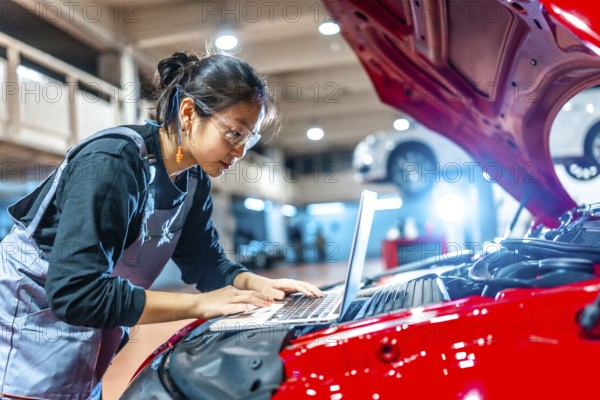 Young female mechanic using a laptop while inspecting a car engine in a professional auto repair