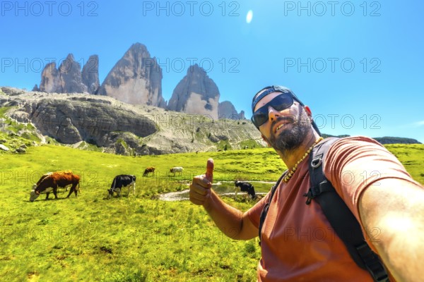 Hiker giving thumbs up while taking a selfie with cows grazing in a meadow with the tre cime di