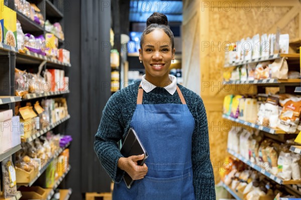 Confident saleswoman smiling and holding tablet, working in organic supermarket with shelves full